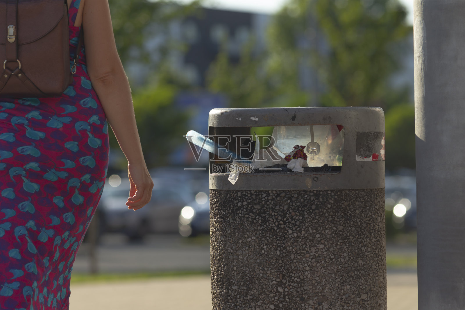 一位女性走过一个垃圾桶，里面有一部手机。照片摄影图片