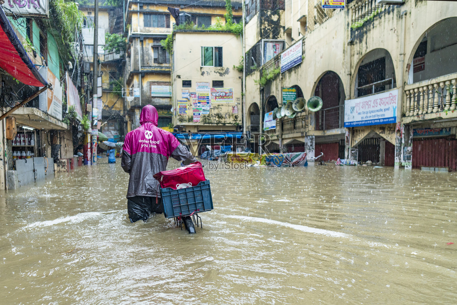 送货员在雨中穿越被淹没的街道。孟加拉国吉大港市的水涝问题屡见不鲜，尤其是在雨季。照片摄影图片