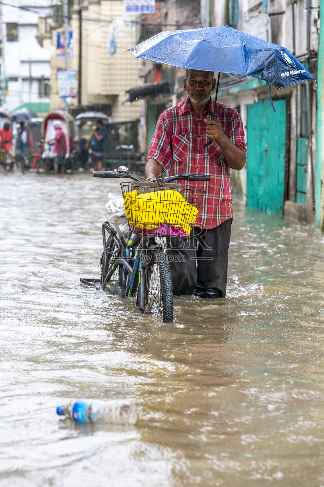 男子在洪水中推着自行车，手持雨伞。水涝是孟加拉国的一个严重问题，尤其是在雨季期间。照片摄影图片