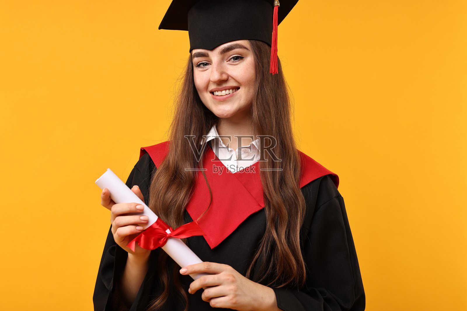 毕业生在橙色背景下手持文凭，面露喜悦之情照片摄影图片