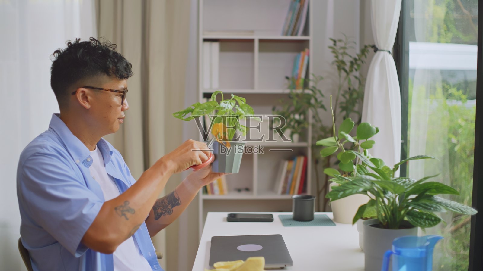 亚洲男子在上班前清理桌子并浇水植物。照片摄影图片