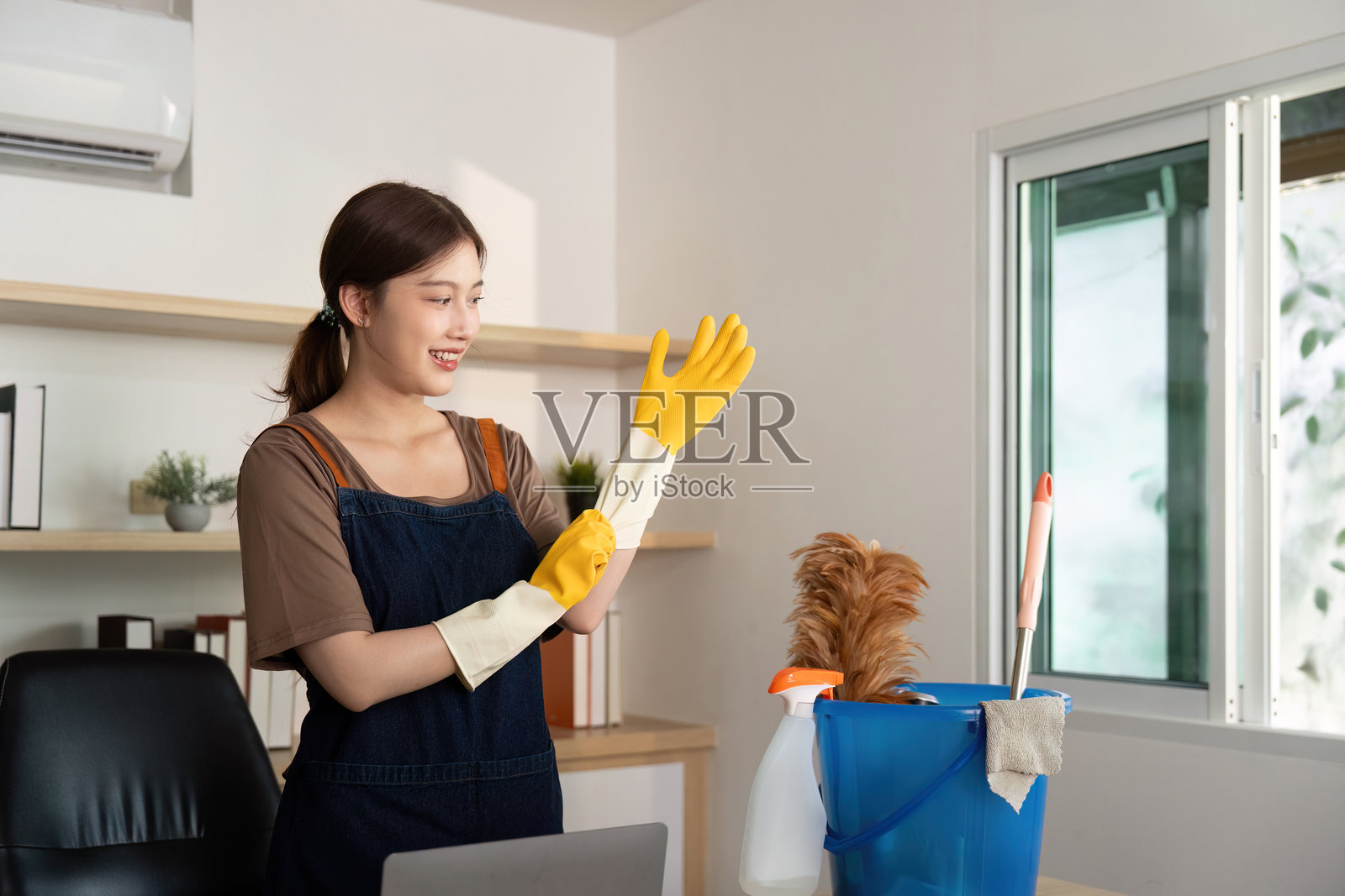 家庭清洁。微笑的女性穿着黄色手套，准备在宠物旁边清理她的工作空间。照片摄影图片