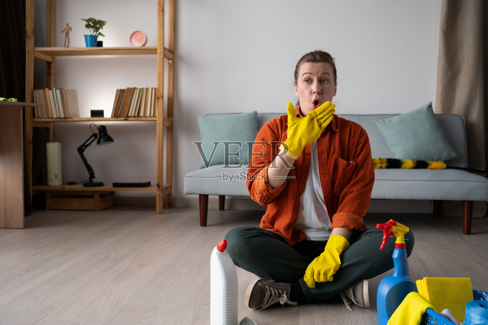 惊讶的家庭主妇坐在地板上，脸上露出惊讶的表情，刚刚打扫完。照片摄影图片