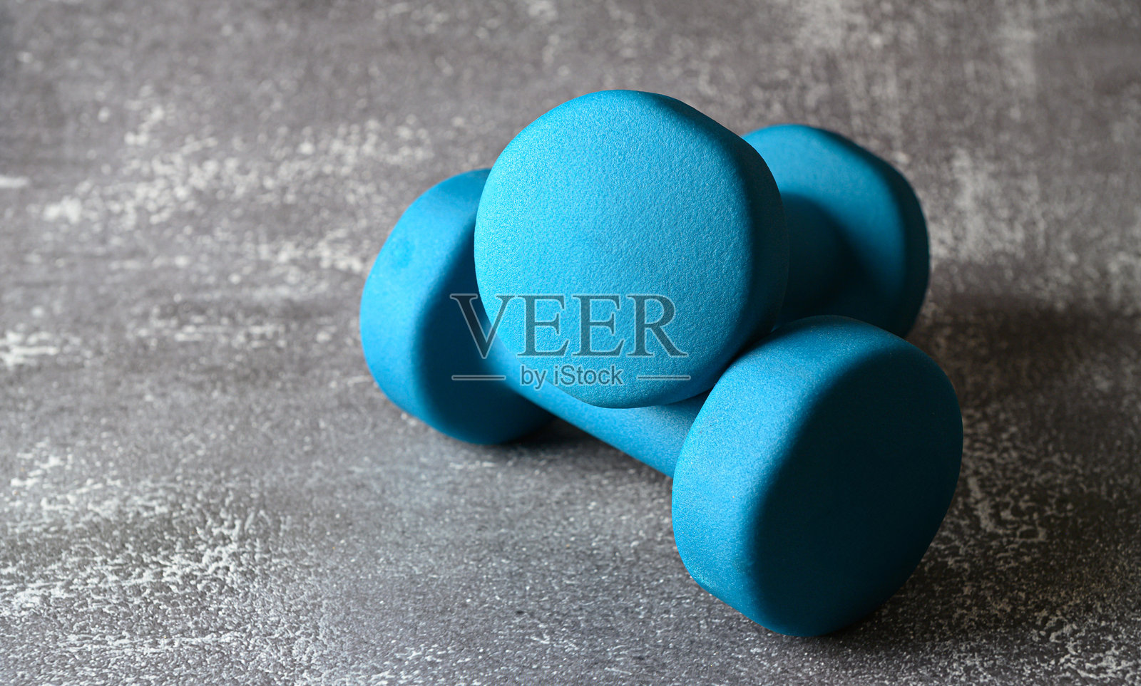 明亮的蓝色氨纶哑铃放在有纹理的表面上，暗示着准备进行健身锻炼或锻炼课程。照片摄影图片