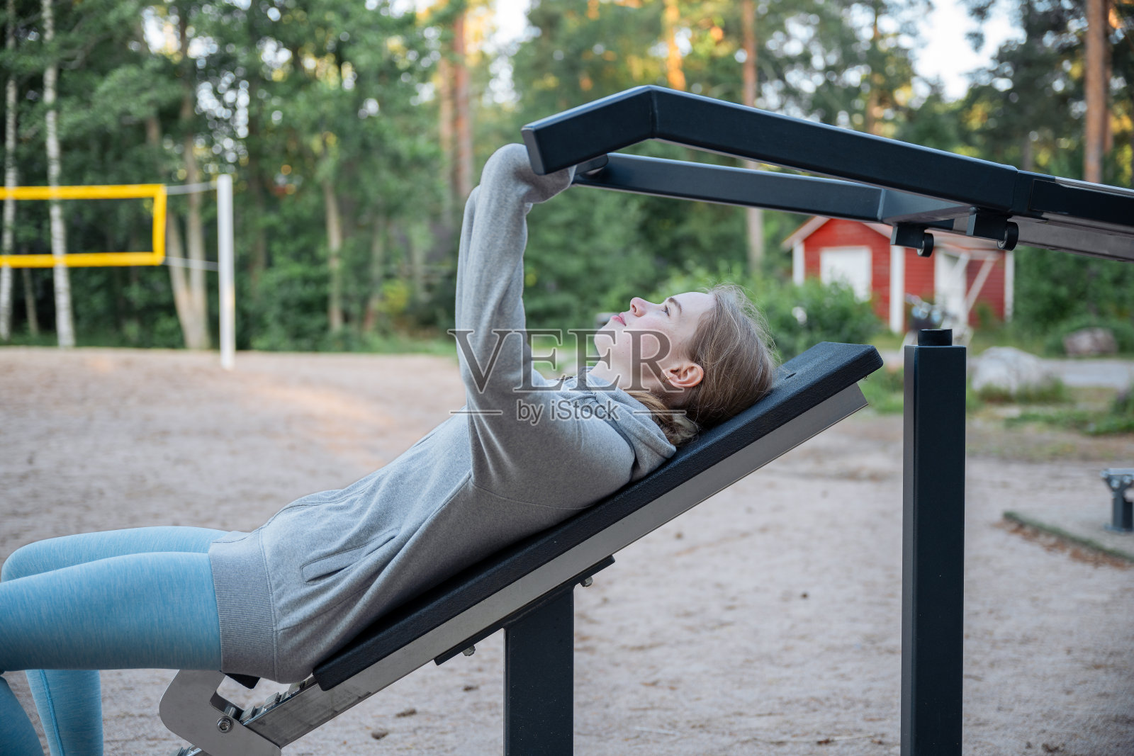 年轻女性在阳光明媚的日子里，在公园的户外健身器械上训练照片摄影图片