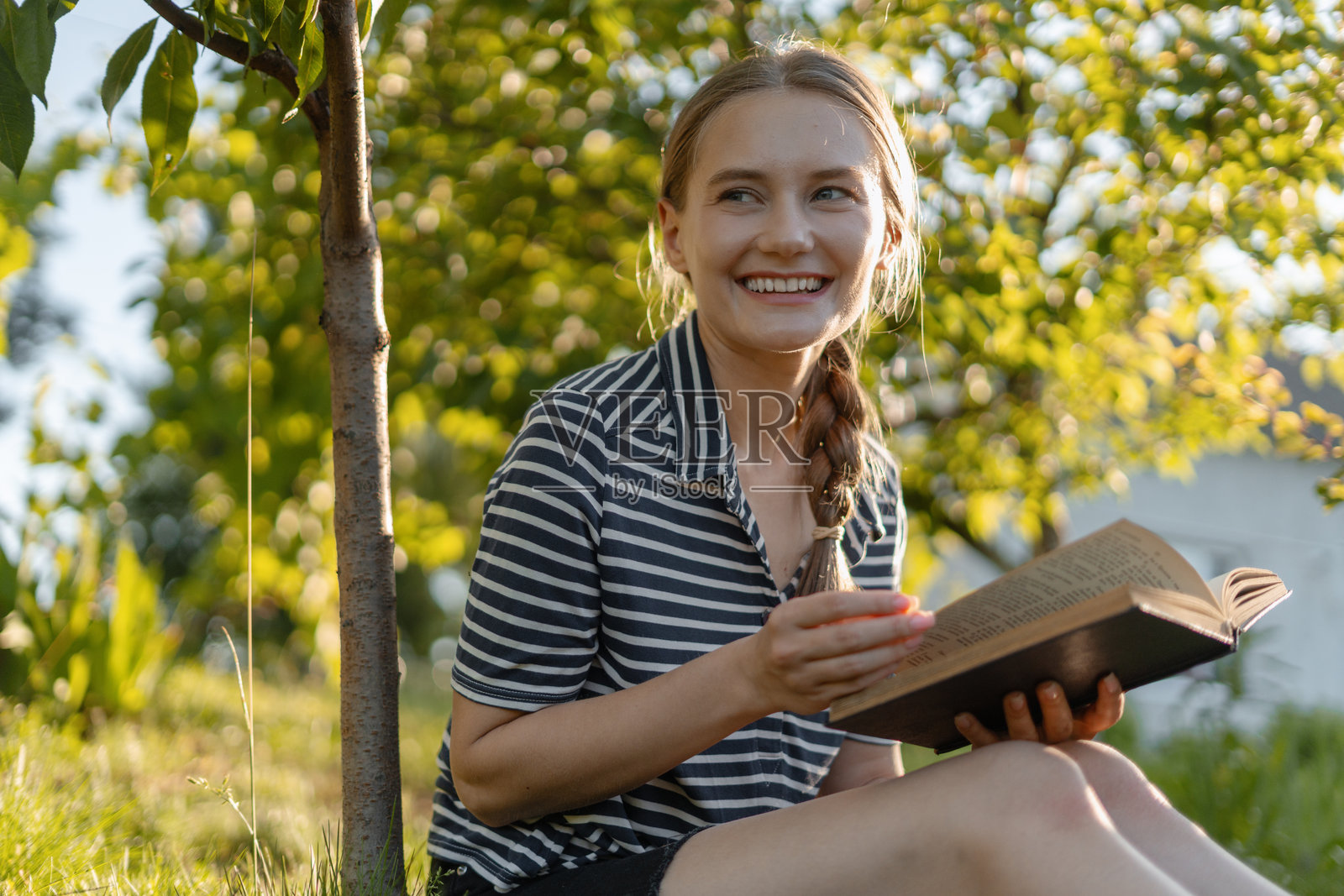年轻女性在花园里微笑着阅读一本书照片摄影图片