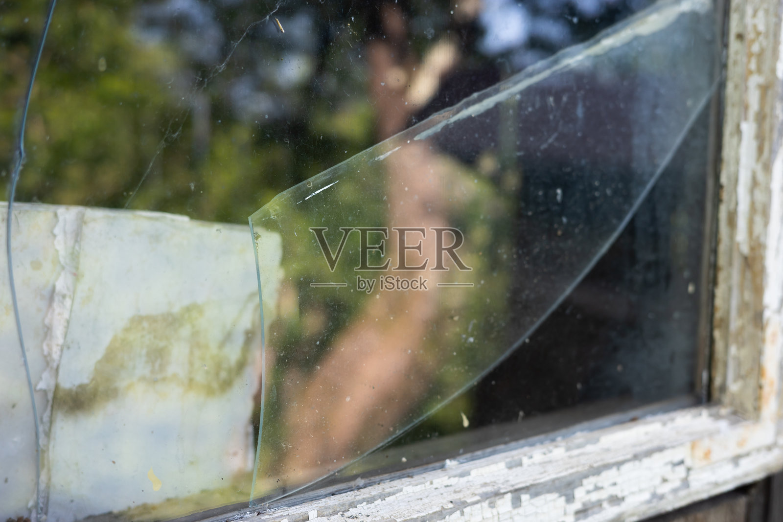 破碎窗户的特写，展示了破碎的玻璃和剥落的油漆。照片摄影图片