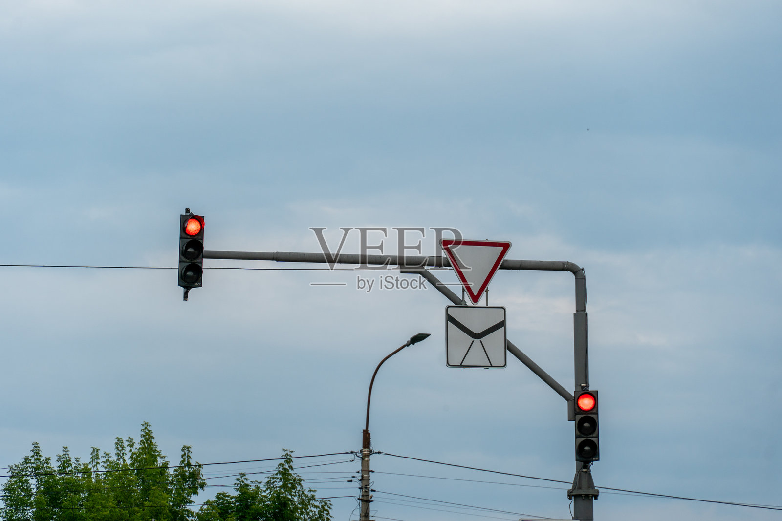 红色交通灯表示车辆在交叉口停驶，而让行标志则指示在阴云天气下接近的交通。照片摄影图片