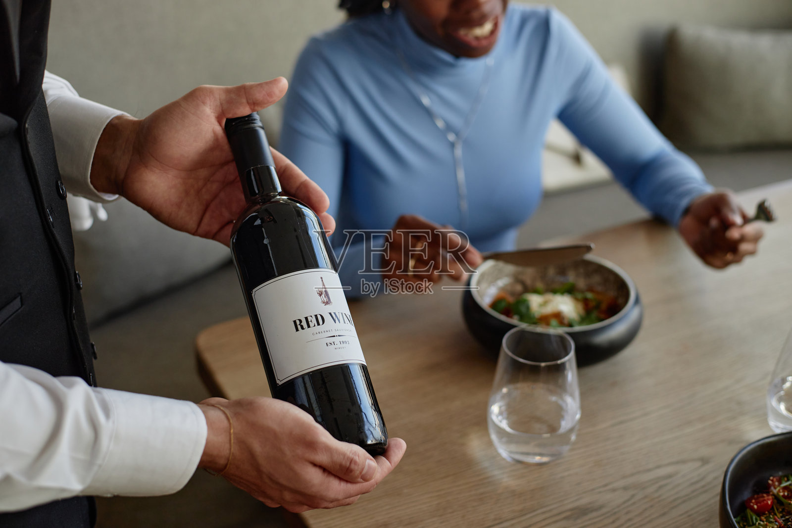 服务员向一位黑人女性客人展示红酒瓶照片摄影图片