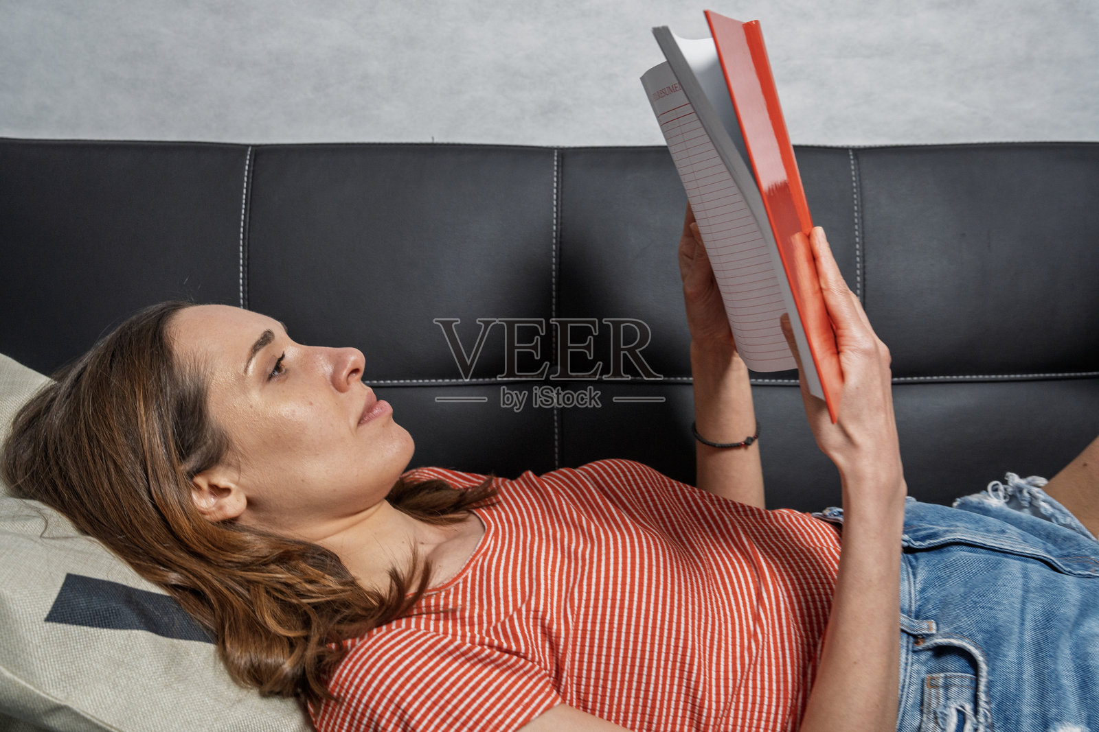 年轻女性在沙发上放松地阅读一本书照片摄影图片