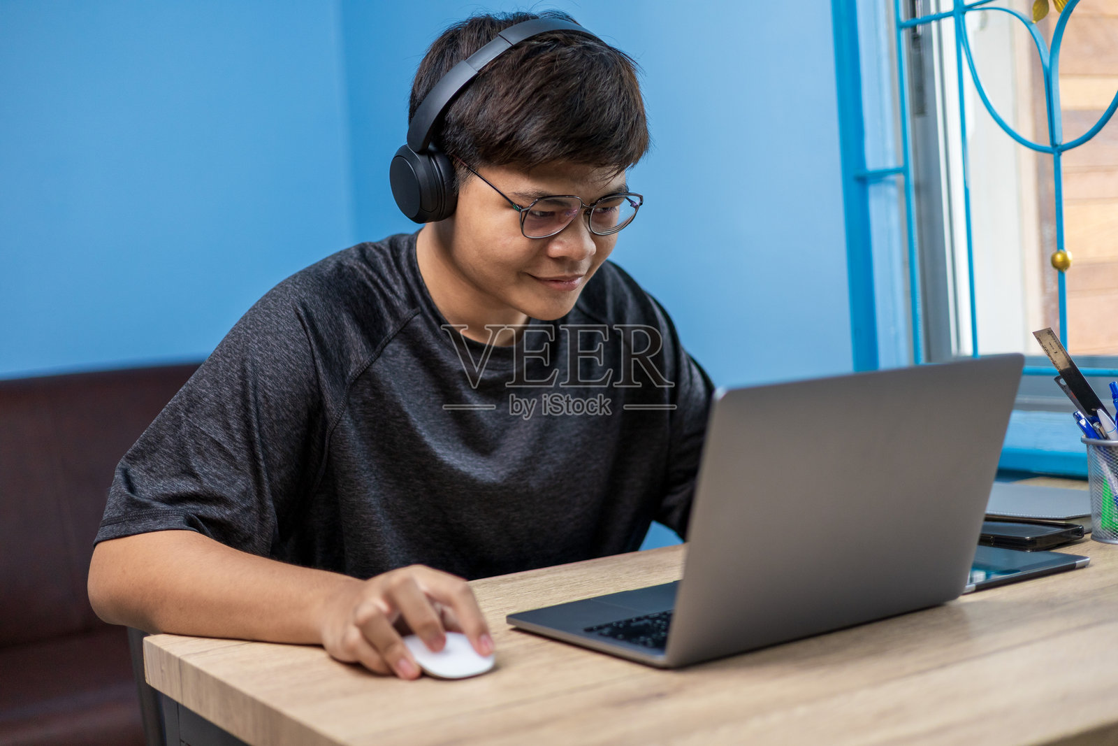 年轻的Z世代成年人坐在椅子上，戴着耳机，使用笔记本电脑在线学习，与导师进行视频会议，搜索教育网页以提升技能，居家学习人工智能。照片摄影图片