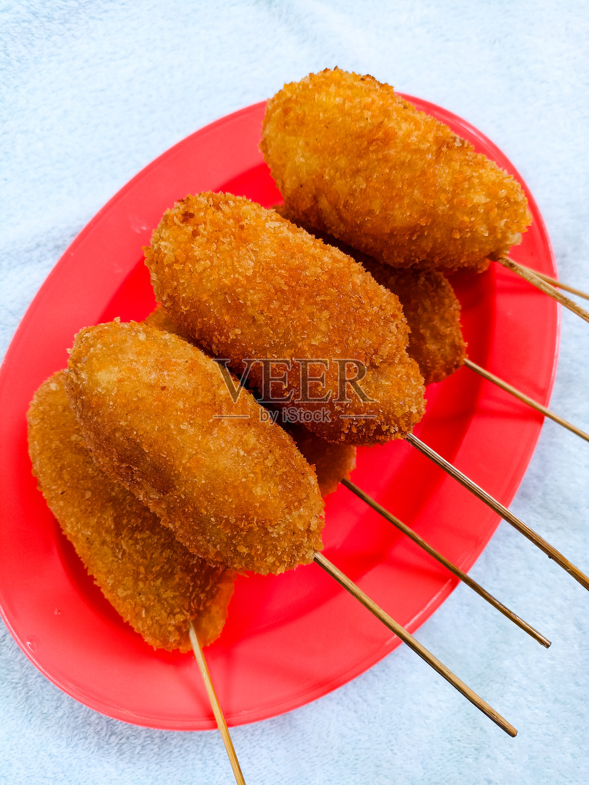 莫扎里拉玉米热狗是韩国一种受欢迎的热狗风味街头食品。它们由面粉制成，里面填充了奶酪，然后油炸而成。它们被放在红色的盘子上。照片摄影图片