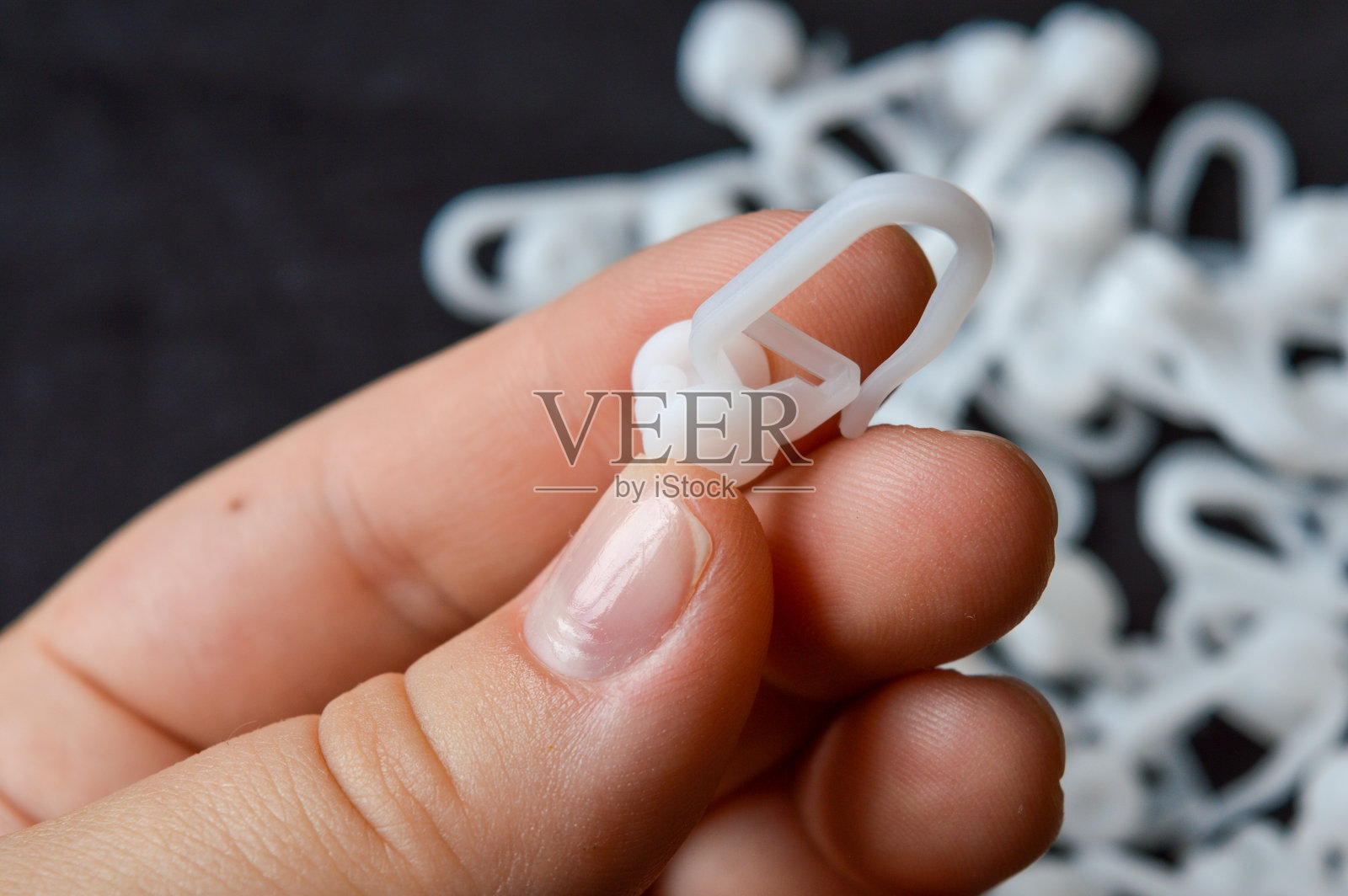 手持白色塑料窗帘钩，带滚轮，特写，背景中有更多钩子，黑色表面上。照片摄影图片