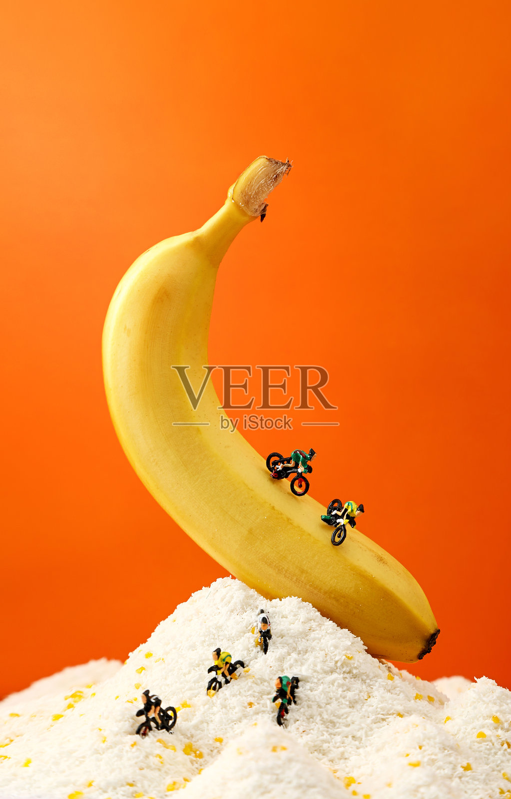 迷你摩托车手骑在巨型香蕉上，迷你人物骑自行车在香蕉上。健康生活方式概念。照片摄影图片