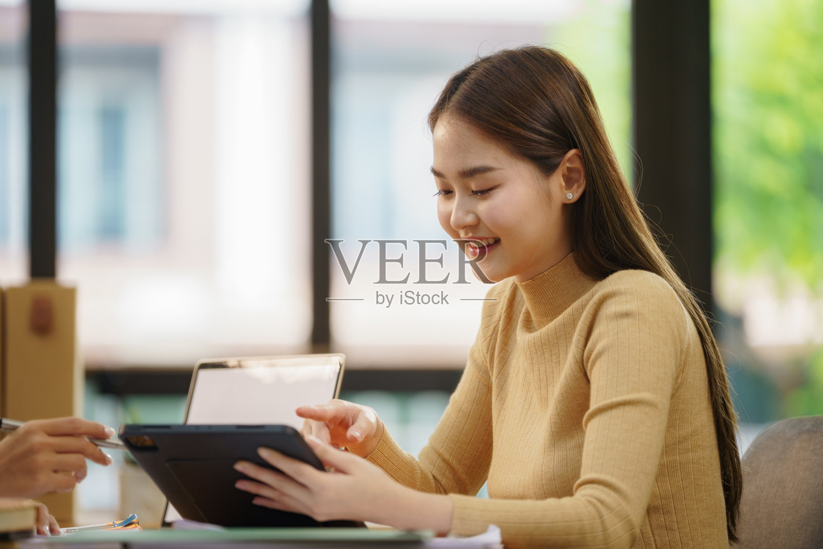 微笑的女性办公室工作人员在办公室查看报告并使用平板电脑。照片摄影图片