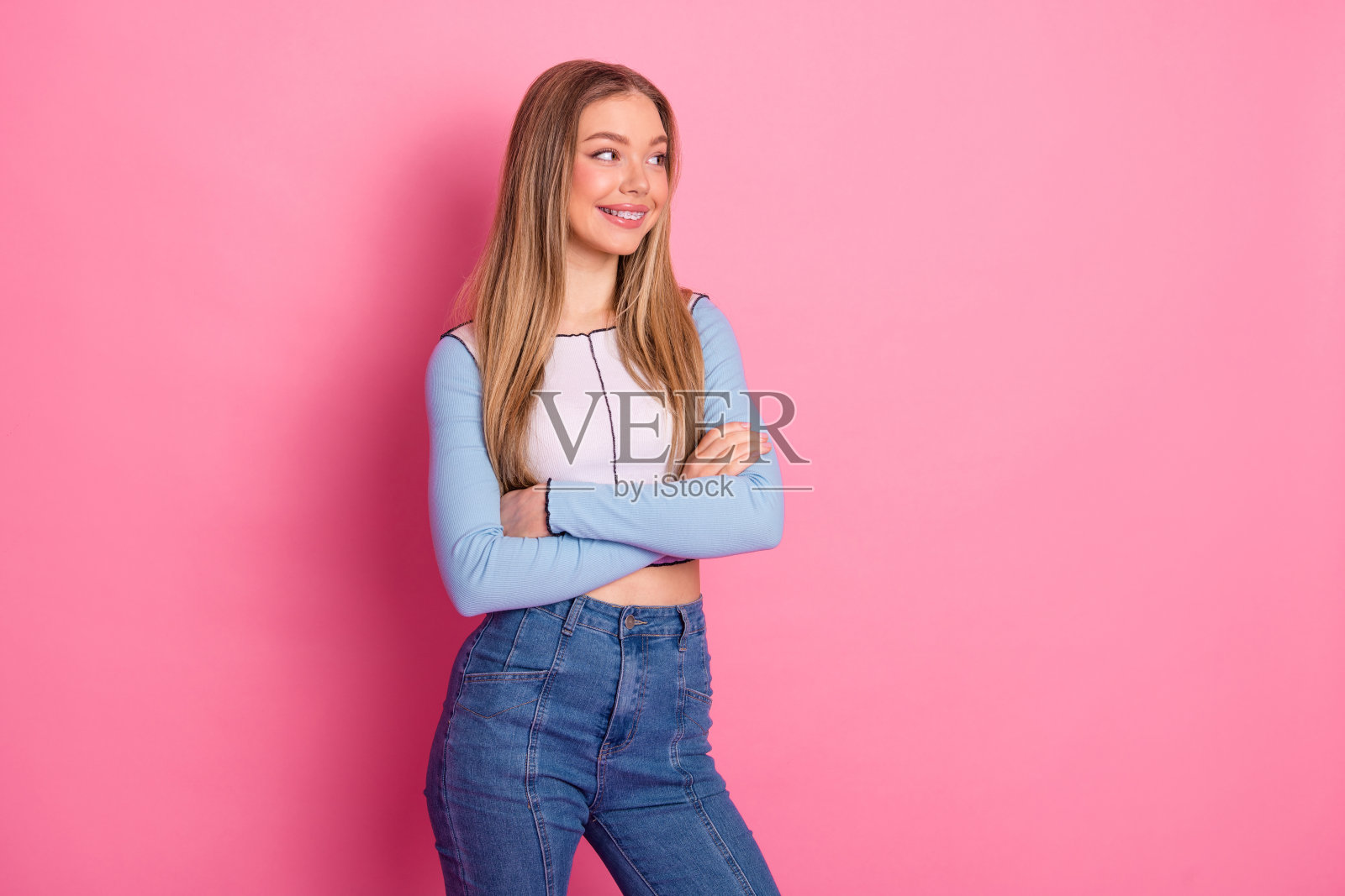 迷人的年轻女性双臂交叉，穿着休闲风格，站在鲜艳的粉色背景前摆姿势照片摄影图片