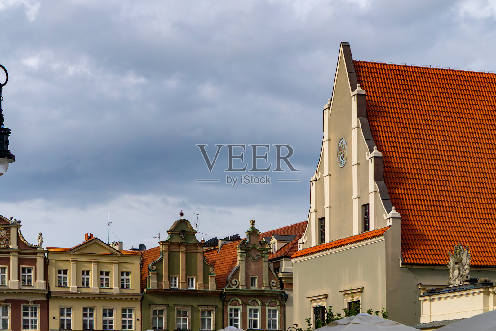 波兹南老市场广场上，历史悠久的联排别墅和一座红屋顶的教堂外观，映衬在阴云密布的天空下。照片摄影图片