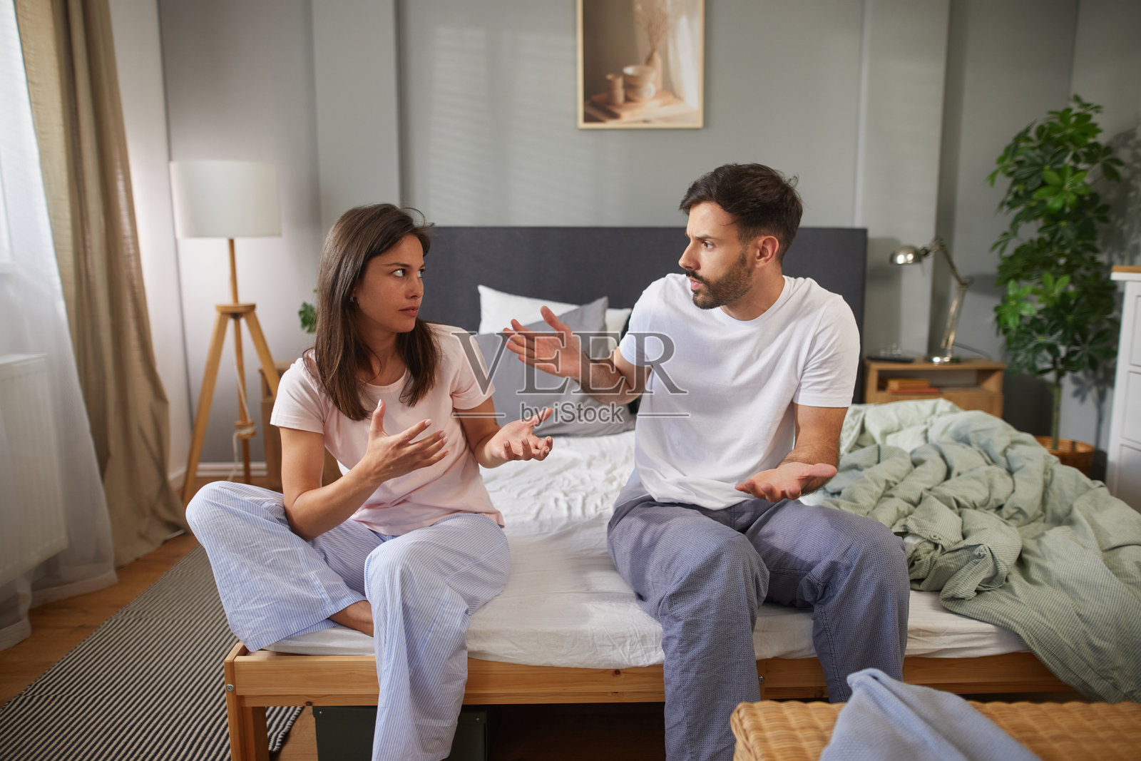 年轻情侣穿着睡衣坐在床上争吵照片摄影图片