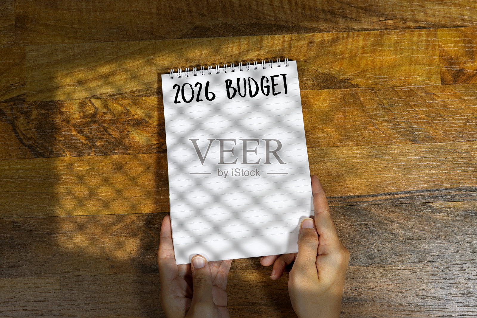 手握笔记本，封面上写着“2026预算”，放在木桌上照片摄影图片