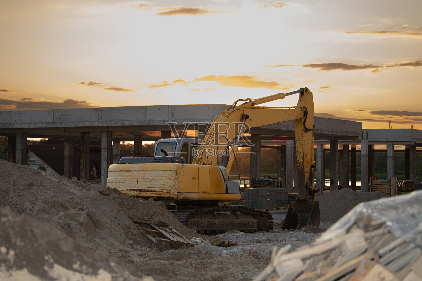 挖掘机在建筑工地上积极挖掘和移动土壤，夕阳在背景中落下，温暖的光辉洒在正在准备的建筑基础上。照片摄影图片