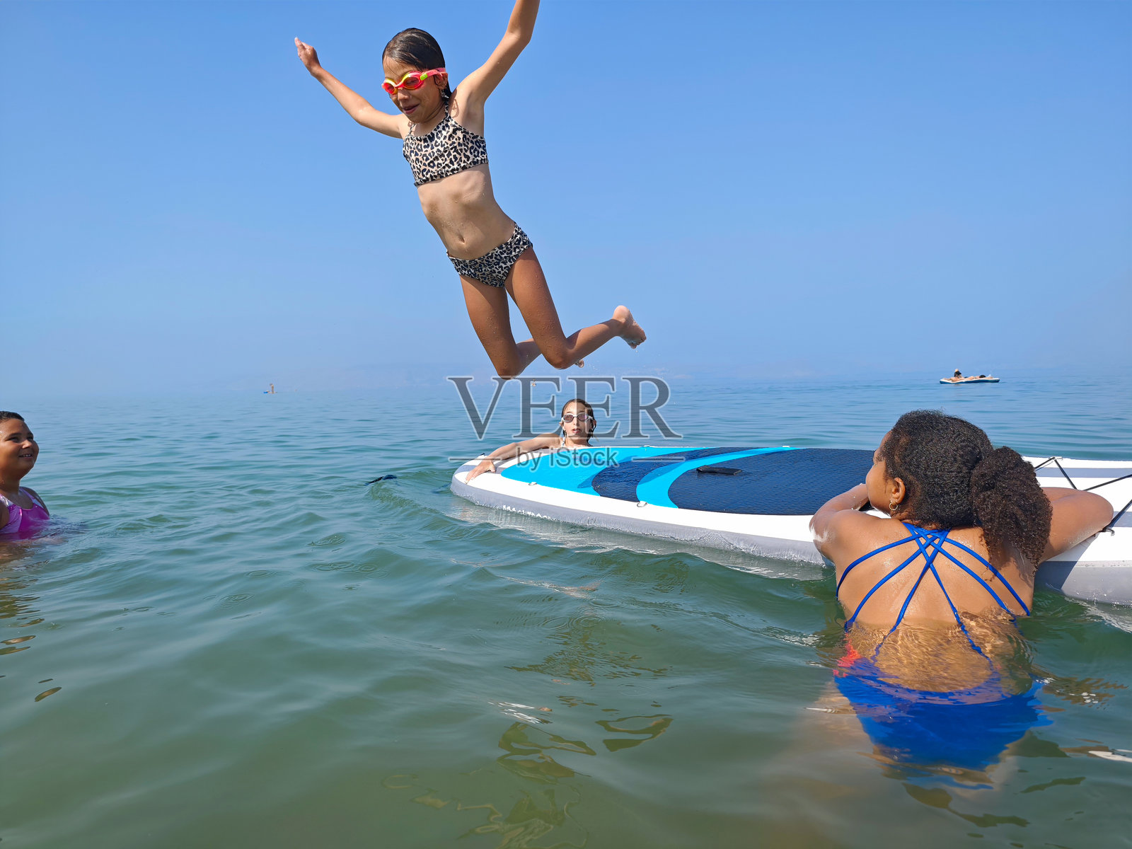 年轻女孩在夏日与朋友们一起从划水板上跳下。照片摄影图片