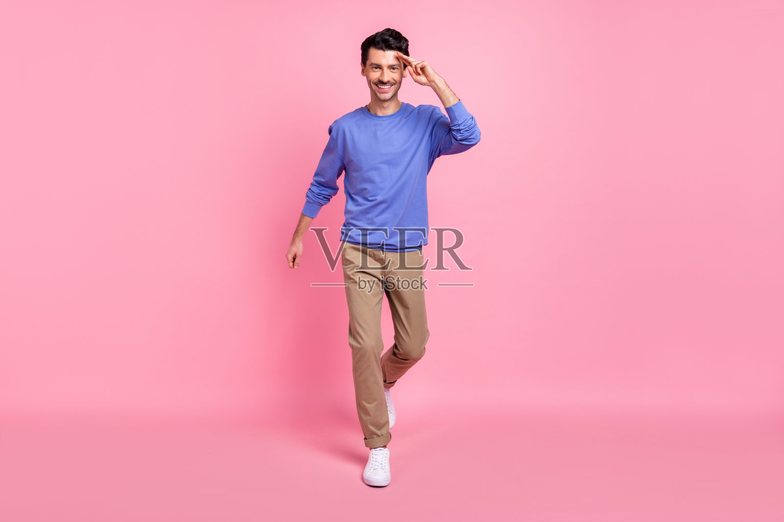 全身照，棕发乐观男士穿着蓝色衬衫、裤子和运动鞋，背景为粉色。照片摄影图片