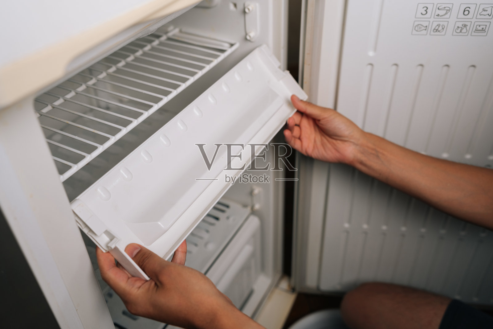 男子准备从冰箱中取出冰块托盘，暗示家庭电器维护的彻底清洁过程。照片摄影图片