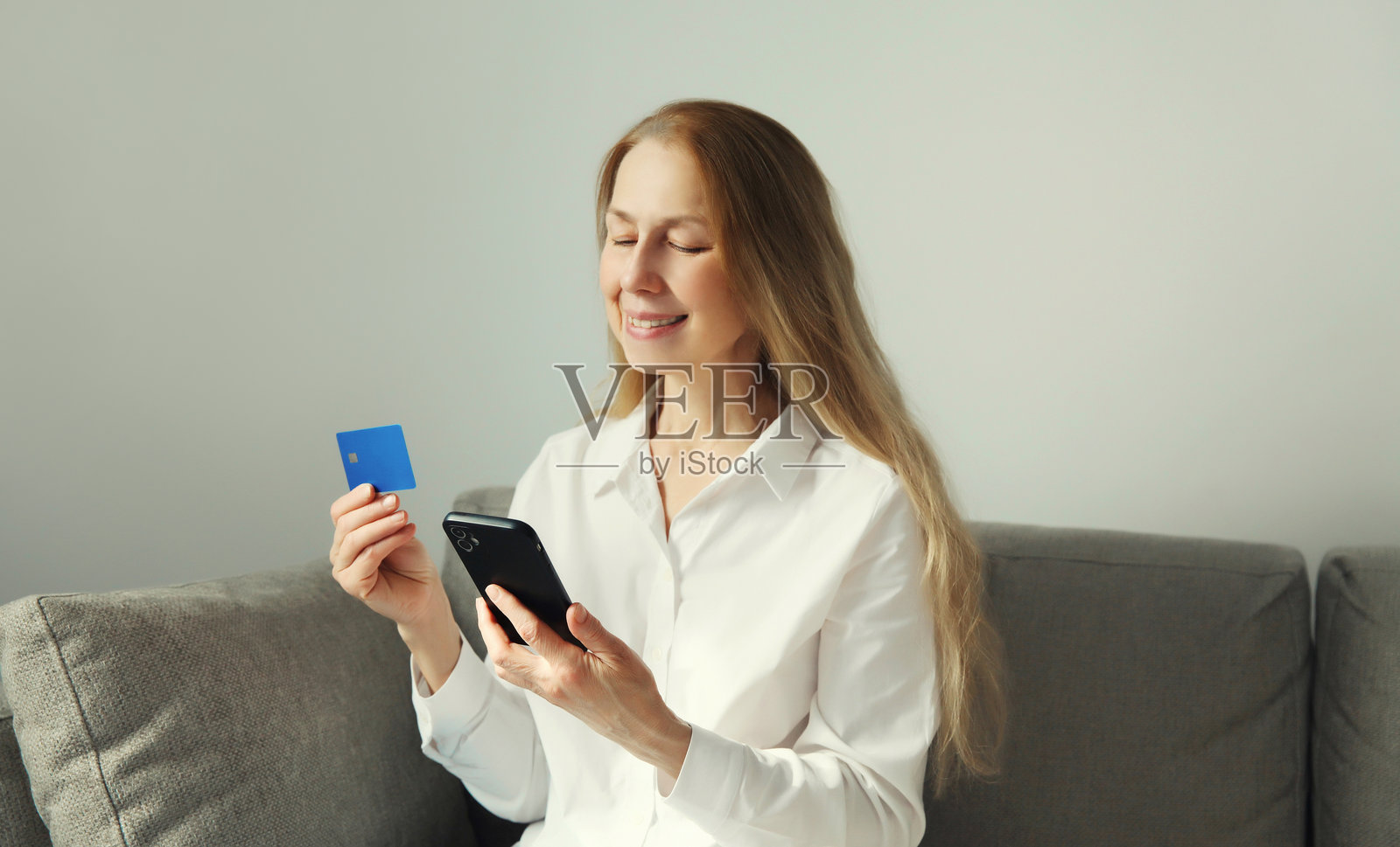 女性手持塑料信用卡，查看手机，在家进行在线购物或订购商品照片摄影图片