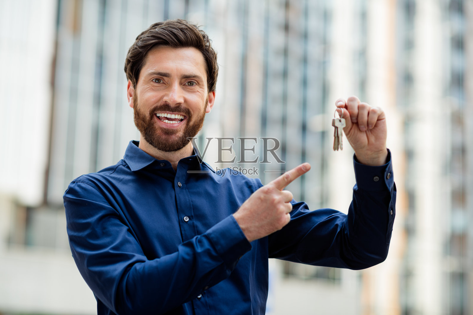 自信的商人手握钥匙，背景是现代城市景观，展示房地产或企业成就照片摄影图片