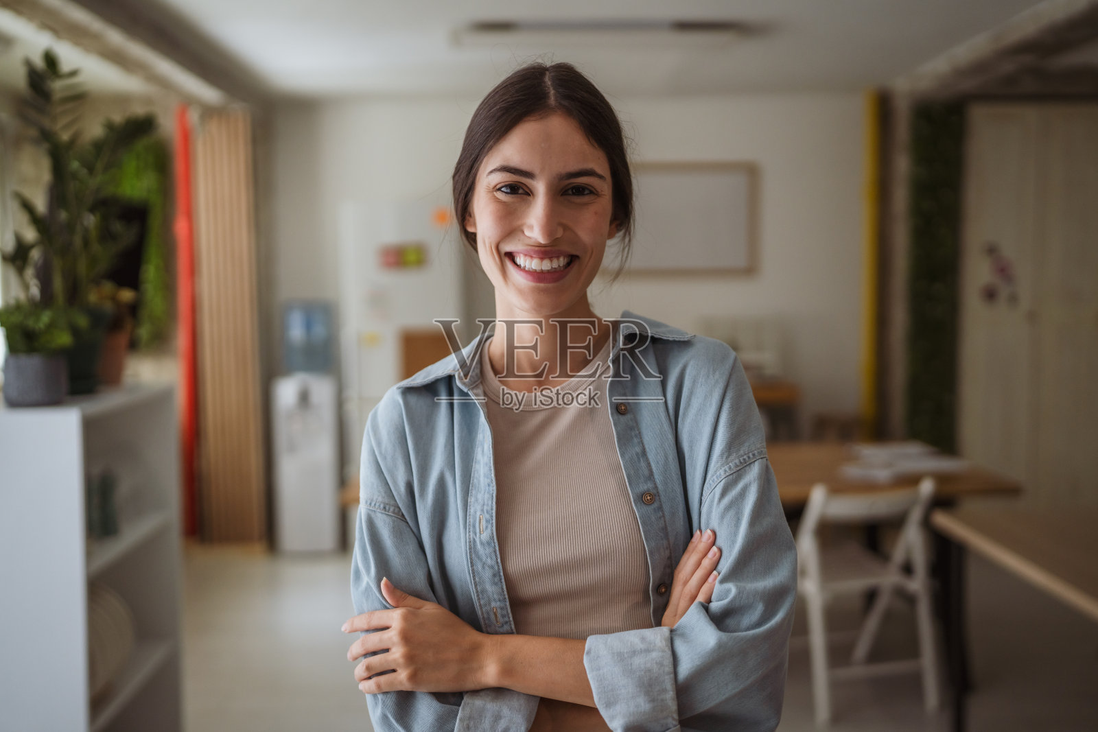 微笑的年轻女商人在现代办公室中双臂交叉的肖像照片摄影图片