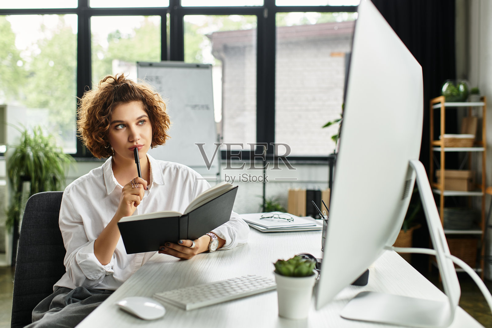 专注的年轻女商人，卷发，在现代办公室从事创意工作照片摄影图片