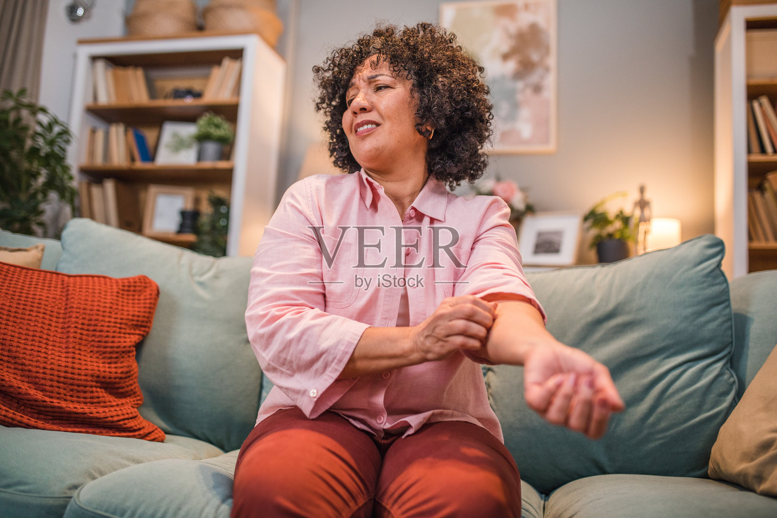 一位多种族女性坐在客厅的沙发上，抓挠着她的手。她的手上有皮疹。照片摄影图片