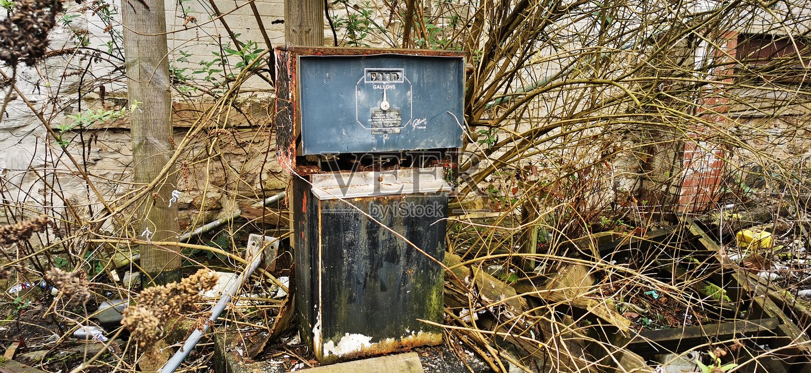 末世风格的无品牌废弃加油站油泵，遗弃的过时古董，周围长满杂草、树枝和碎片。照片摄影图片