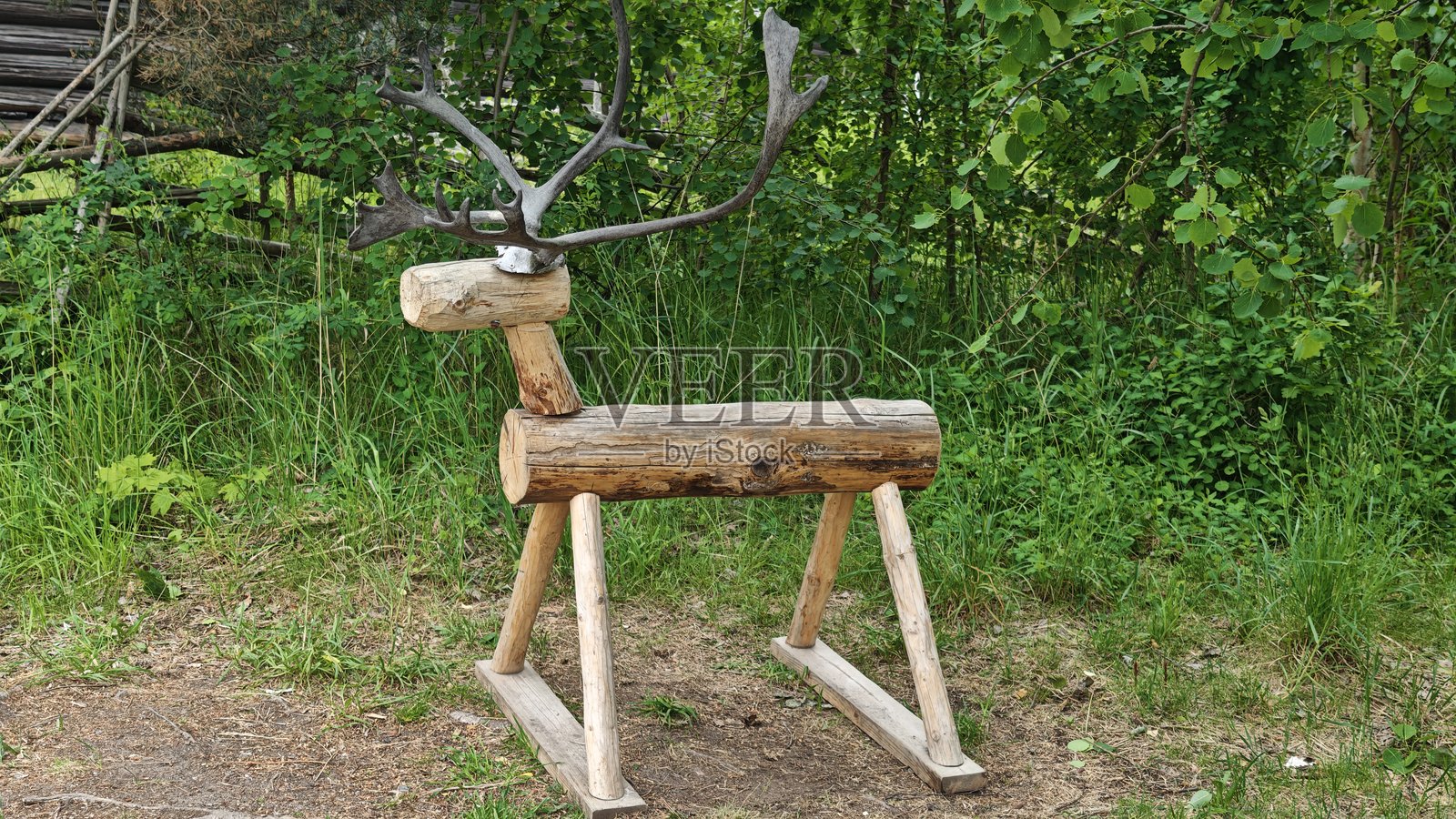 手工制作的木制鹿玩具，带有真实的鹿角，站在草地上，背景是森林。照片摄影图片