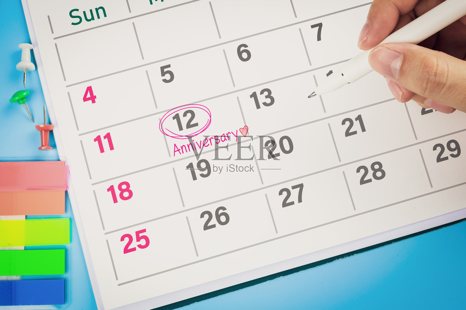 特写镜头显示手用笔在日历上画粉色圆圈，写上“周年纪念”和心形图案。婚礼周年纪念的概念。照片摄影图片