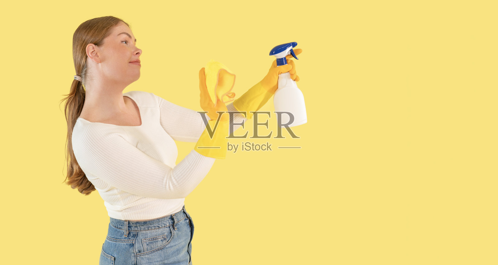 年轻女性在鲜艳的黄色背景下准备清洁，手持喷雾瓶和布。照片摄影图片