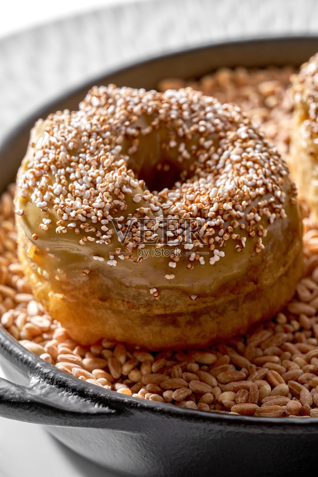 两款创意咸味甜甜圈，配有肉酱和酥脆的配料，放在铸铁煎锅中的谷物床上。照片摄影图片