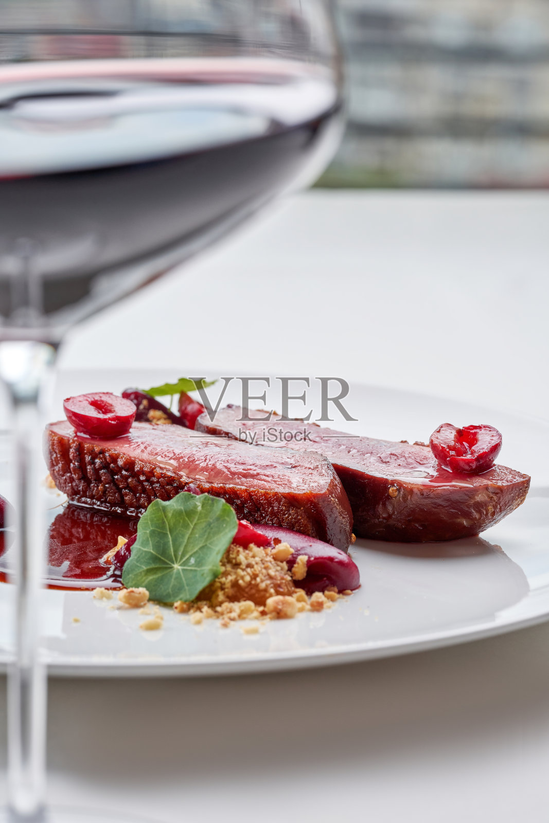 一盘精致的美食，完美烹饪的鸭胸肉配樱桃、浓郁的酱汁和脆皮，前景中搭配一杯红酒。照片摄影图片