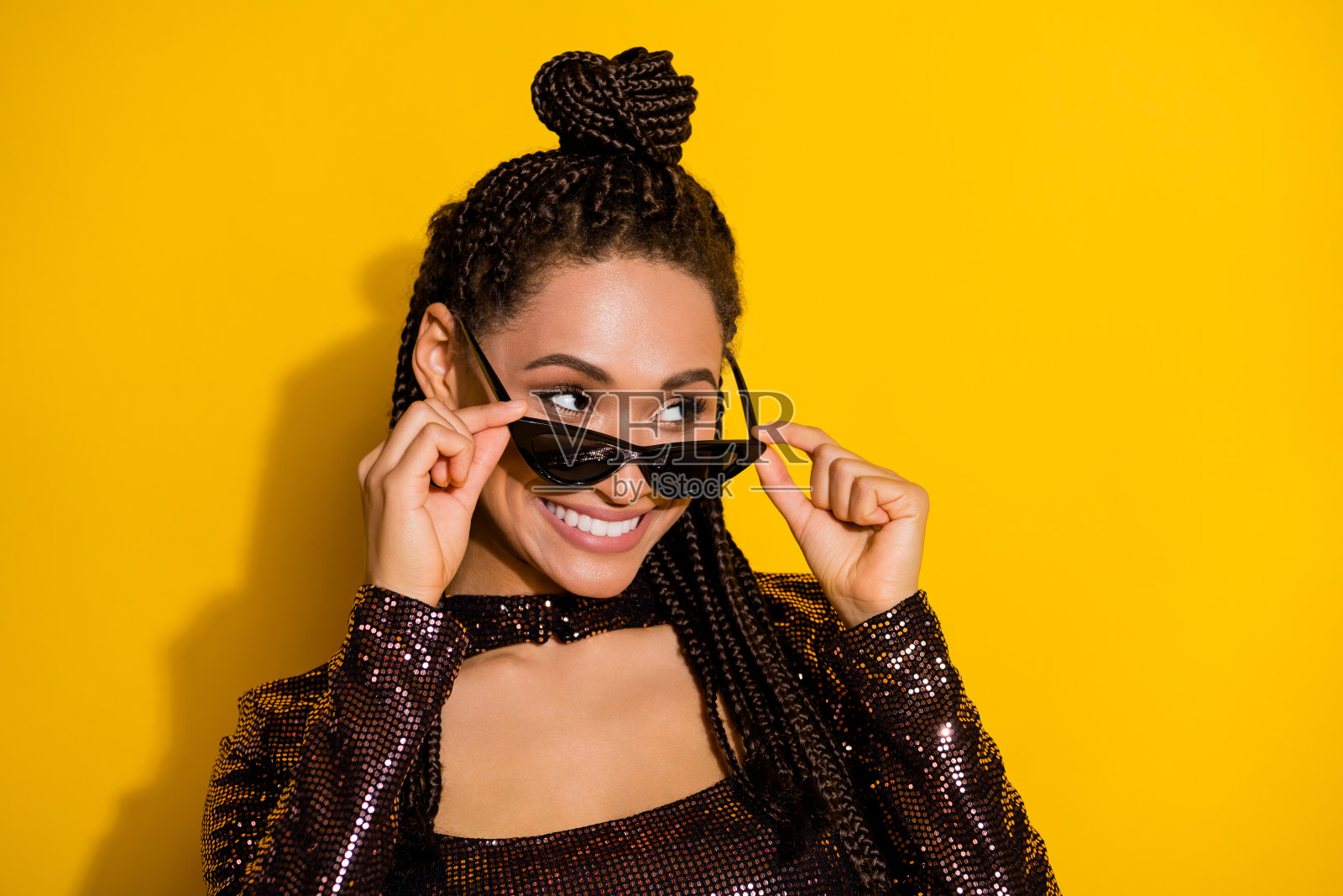 迷人调皮的女士摘下眼镜，望向空旷的空间，佩戴着太阳镜，穿着光泽感衬衫，背景为黄色。照片摄影图片
