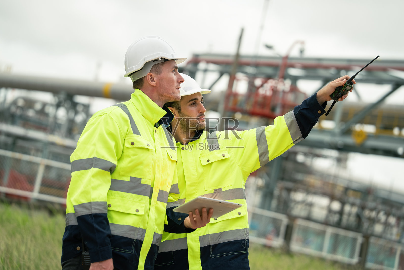 工程师在石油化工行业或炼油厂工地上，通过数字平板电脑查看工作监控，并与同事使用对讲机交谈。照片摄影图片