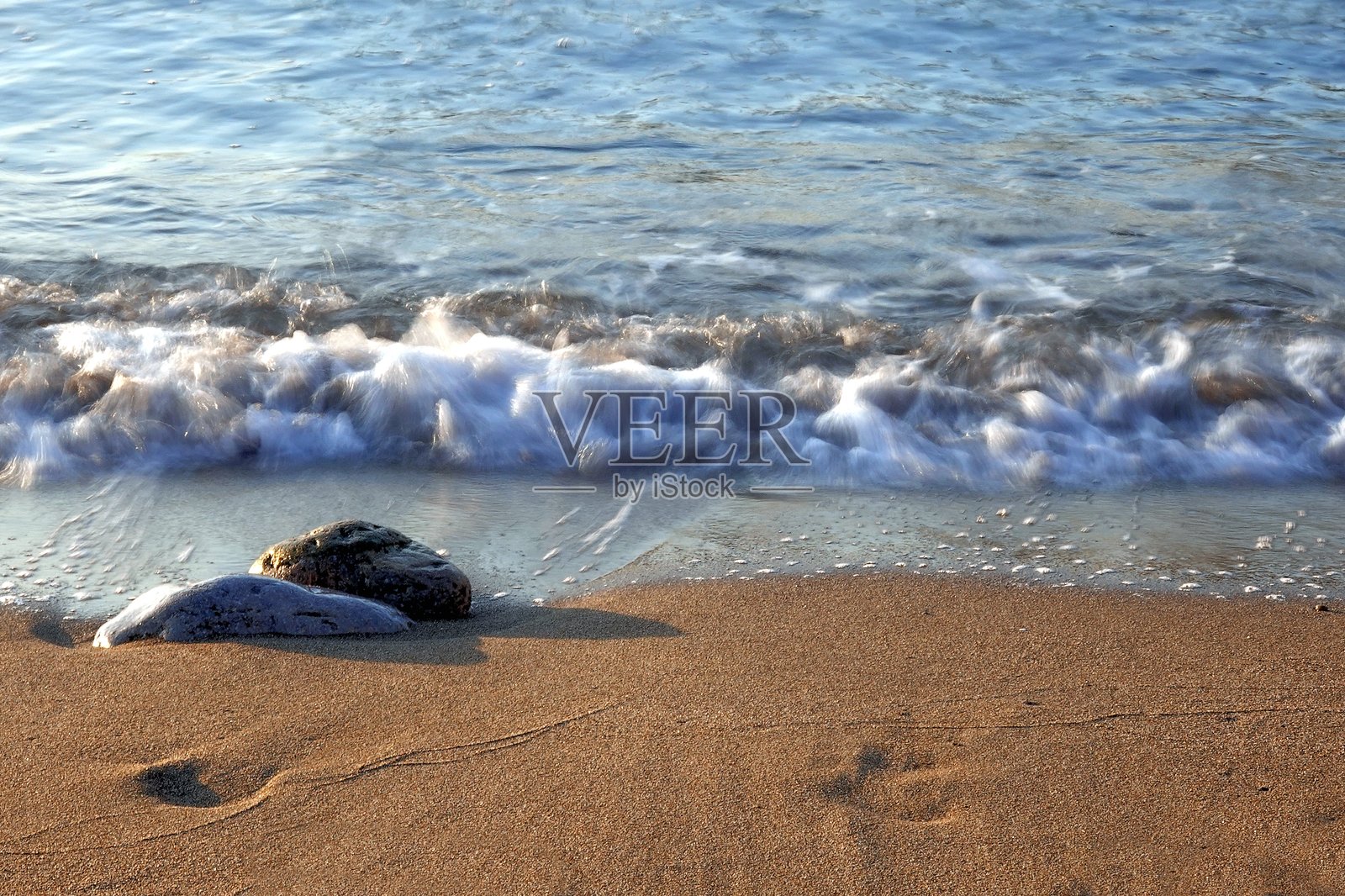 黎明时分的海浪轻柔地抚摸着海岸的石头。照片摄影图片