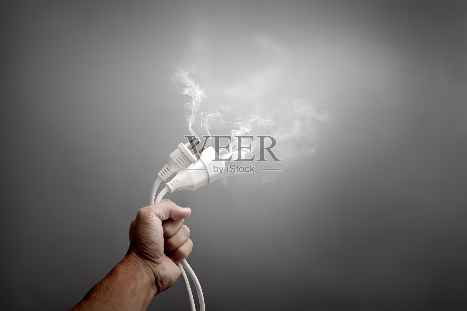 手握着冒烟的电源线末端照片摄影图片