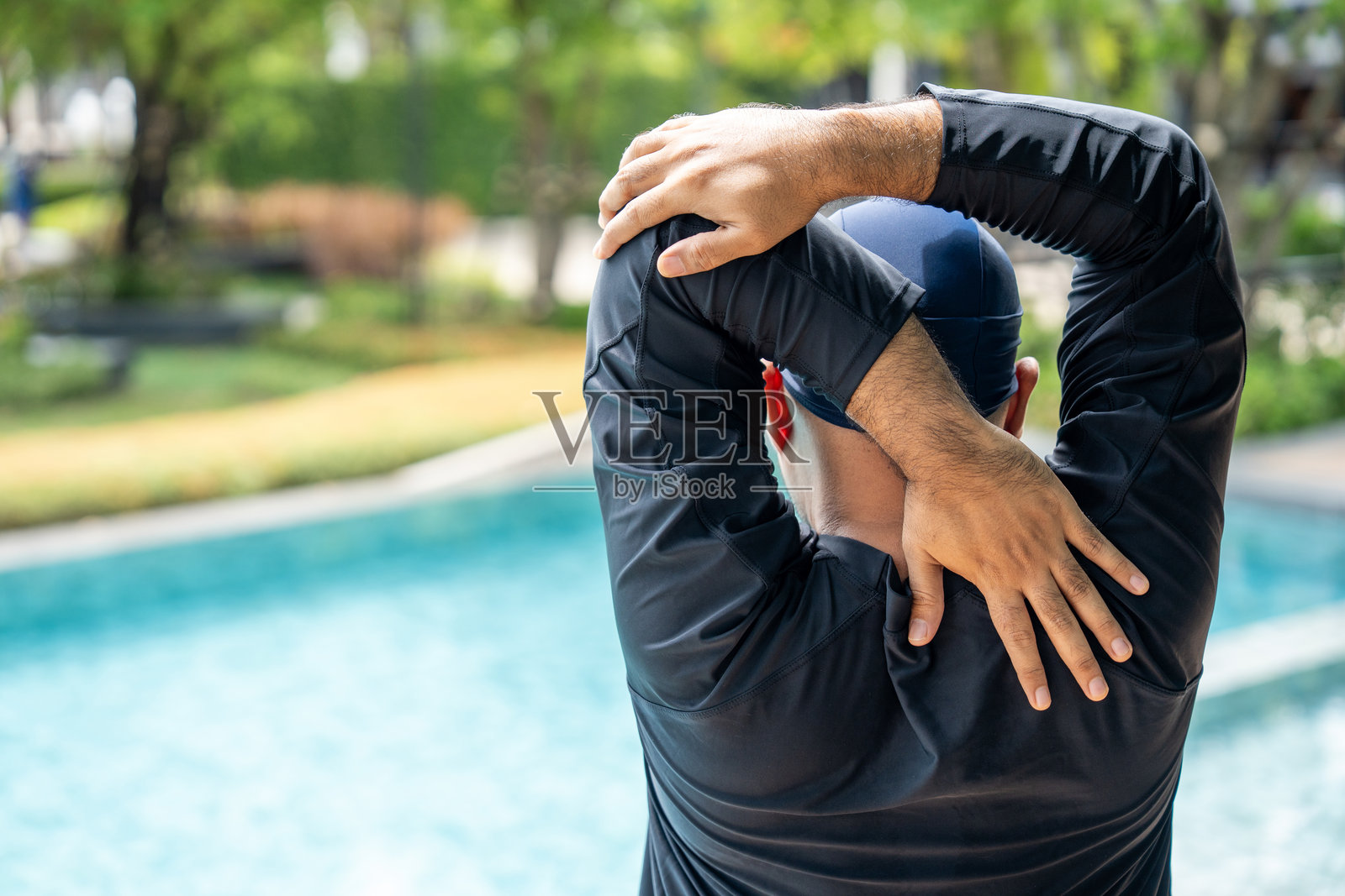 一位穿着黑色泳衣的人在泳池边伸展身体，为游泳做准备。这张图片传达了热身和保持健康积极生活方式的重要性。照片摄影图片