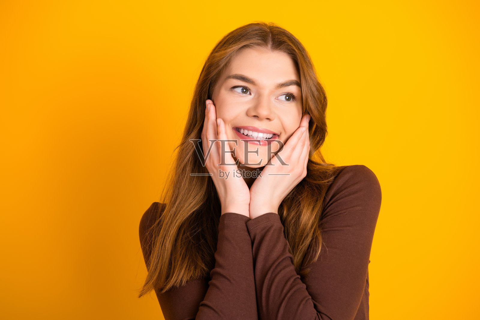 穿着休闲服的年轻女性在明亮的黄色背景前微笑，散发着快乐和魅力。照片摄影图片