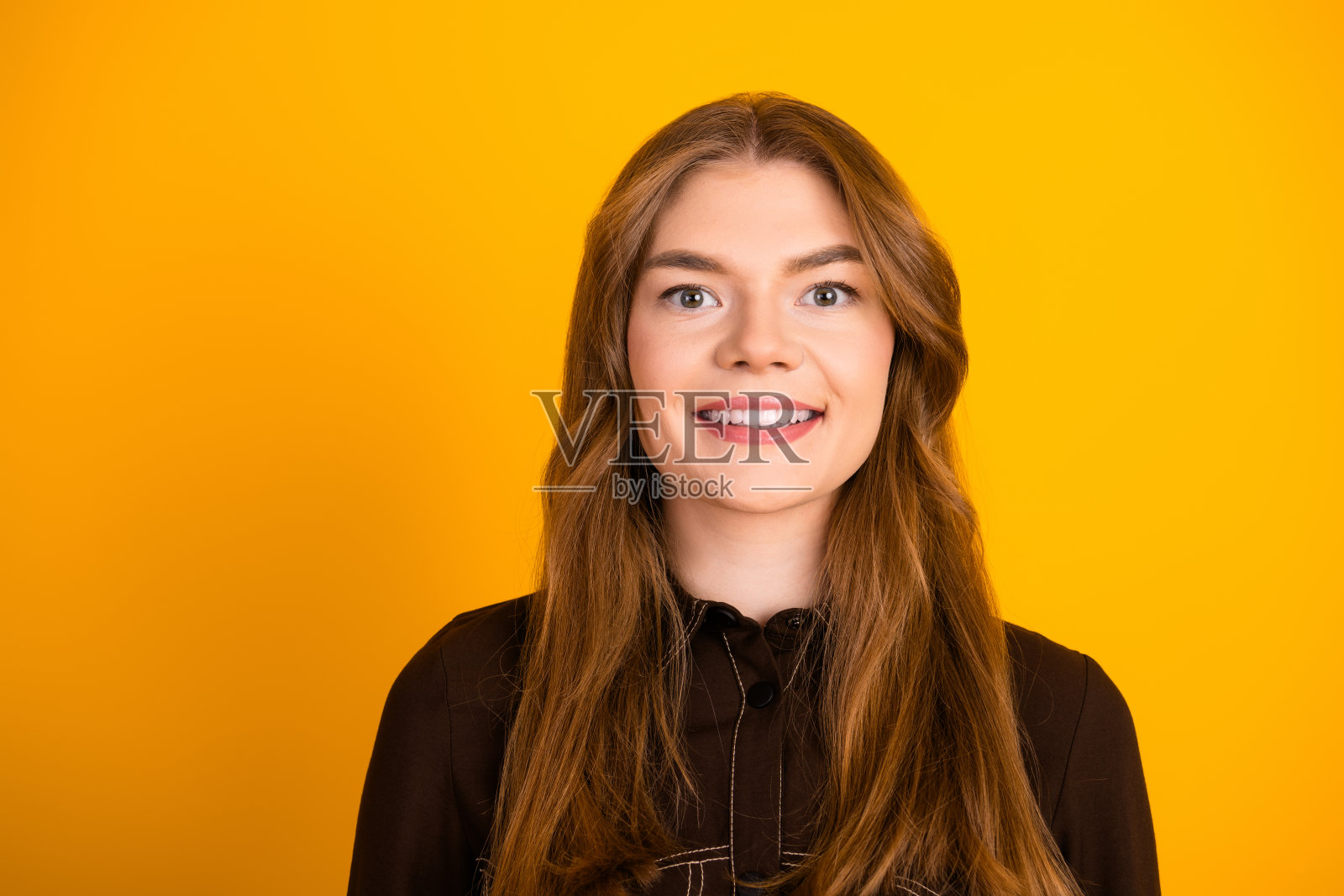 一位年轻女性的肖像，长棕色头发，迷人的微笑，穿着时尚休闲服，背景为黄色。照片摄影图片