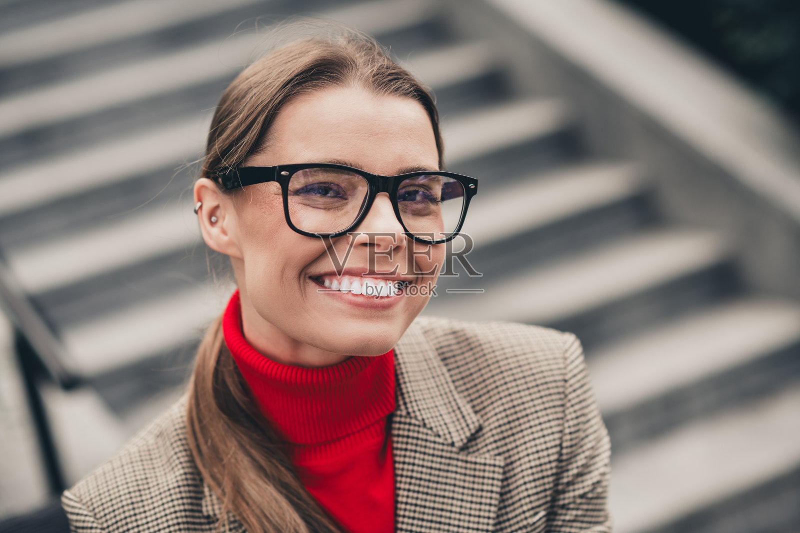 自信的年轻女商人在城市中心的户外穿着时尚夹克和眼镜，温暖地微笑。照片摄影图片