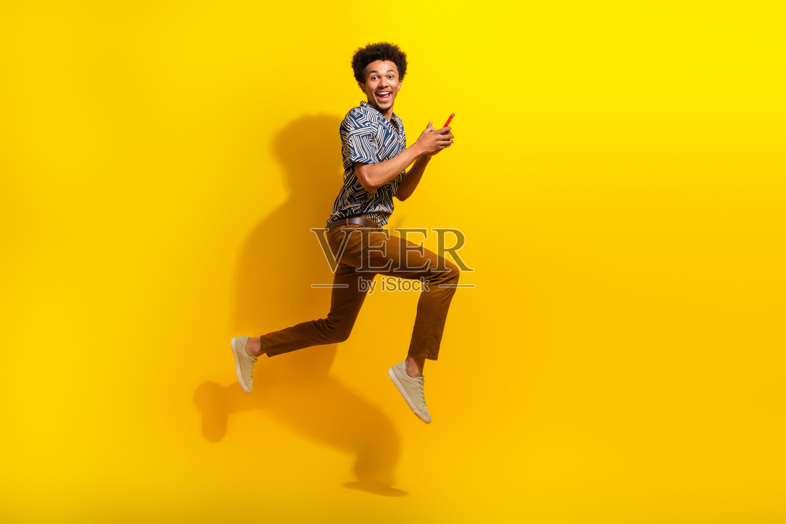 兴奋的年轻人穿着时尚的服装，在充满活力的黄色背景下快乐地跳跃，表达着喜悦和活力。照片摄影图片