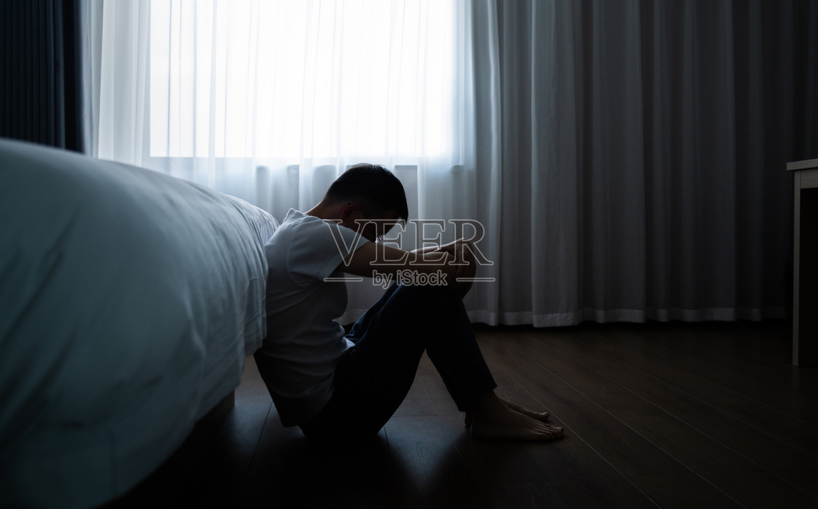 沮丧的男人坐在卧室地板上照片摄影图片