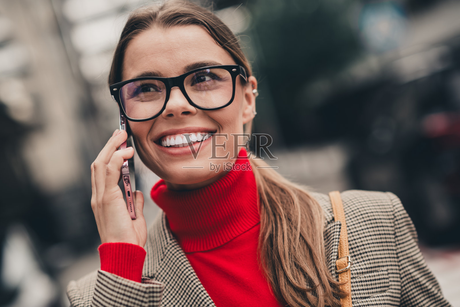 年轻职业女性穿着时尚都市服装，正在用智能手机通话，散发出自信与魅力。照片摄影图片