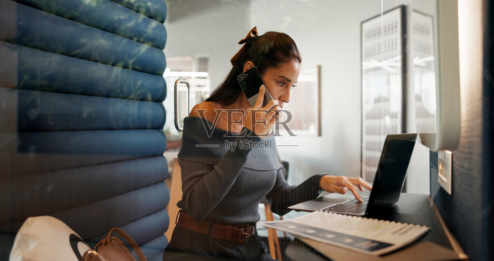 女性在办公室隔间中使用笔记本电脑和手机进行财务咨询、帮助或保险政策的通话。女性，可能是会计师，正在通过手机或电脑进行财务或协助的交流。照片摄影图片